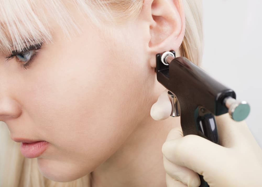 Woman having ear piercing process with special equipment in beauty center by medical worker.