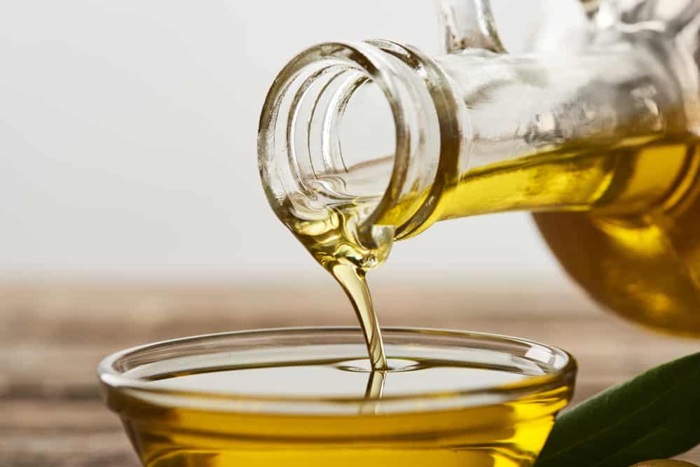 Pouring olive oil from bottle into glass bowl on grey background